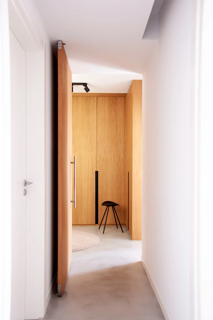 Bright corridor with continuous pale flooring, white walls and warm full-height timber joinery at the far end.