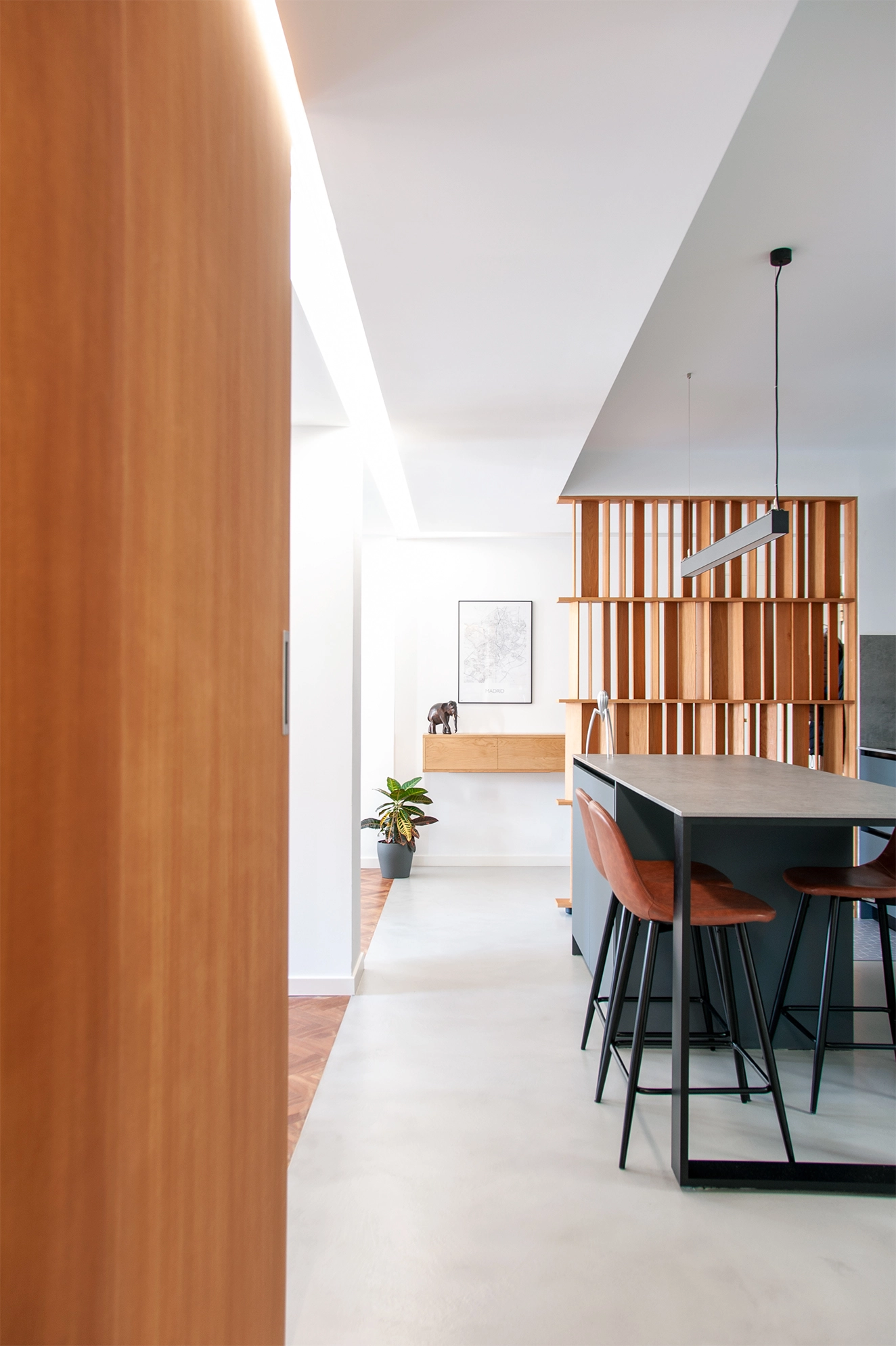Open kitchen and dining area with dark cabinetry, timber screening, bar stools and indirect daylight.