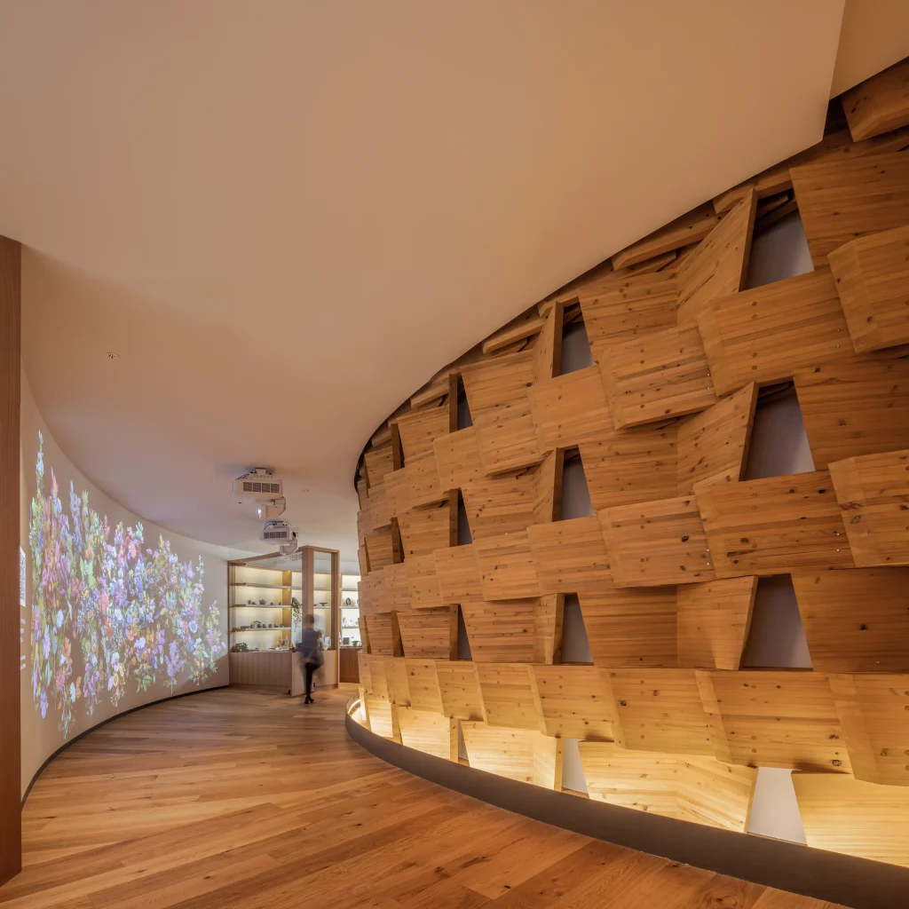 Curved interior passage with stacked timber modules on one side and a projected display on the opposite wall.