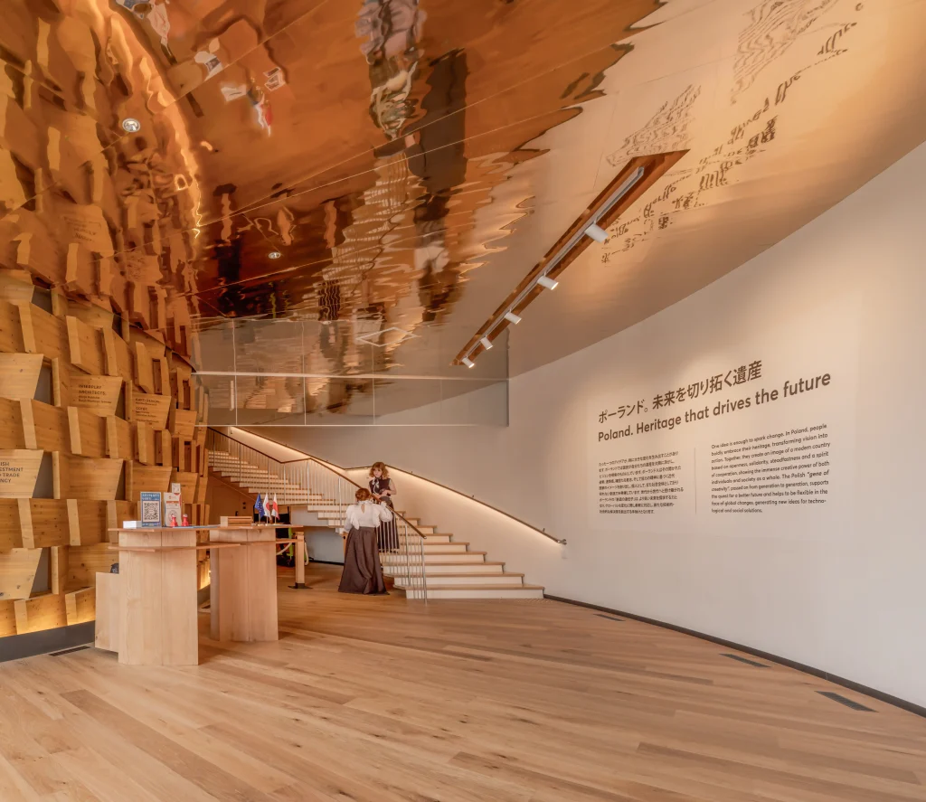 Entrance to the pavilion exhibition route, combining timber wall modules, a reflective ceiling and introductory graphics.