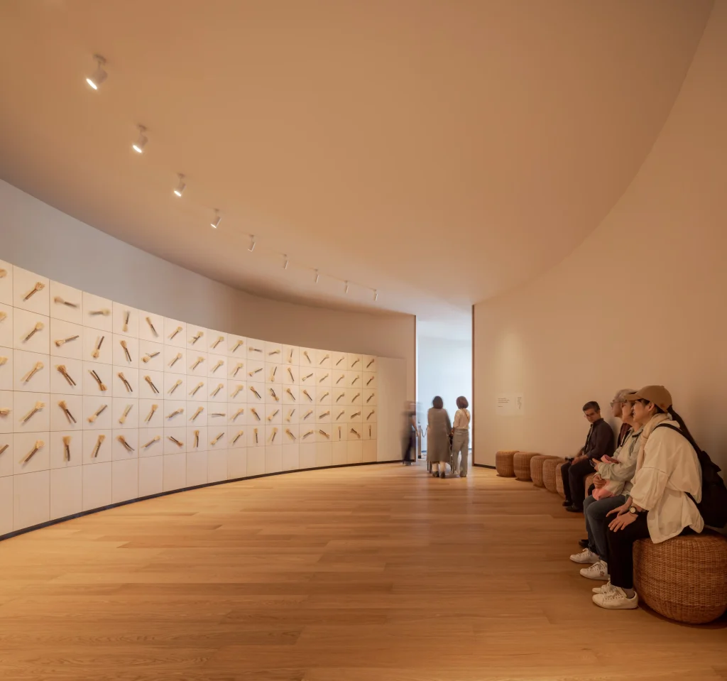 Curved exhibition gallery inside the Poland Pavilion, with a pale display wall, timber floor and seating.