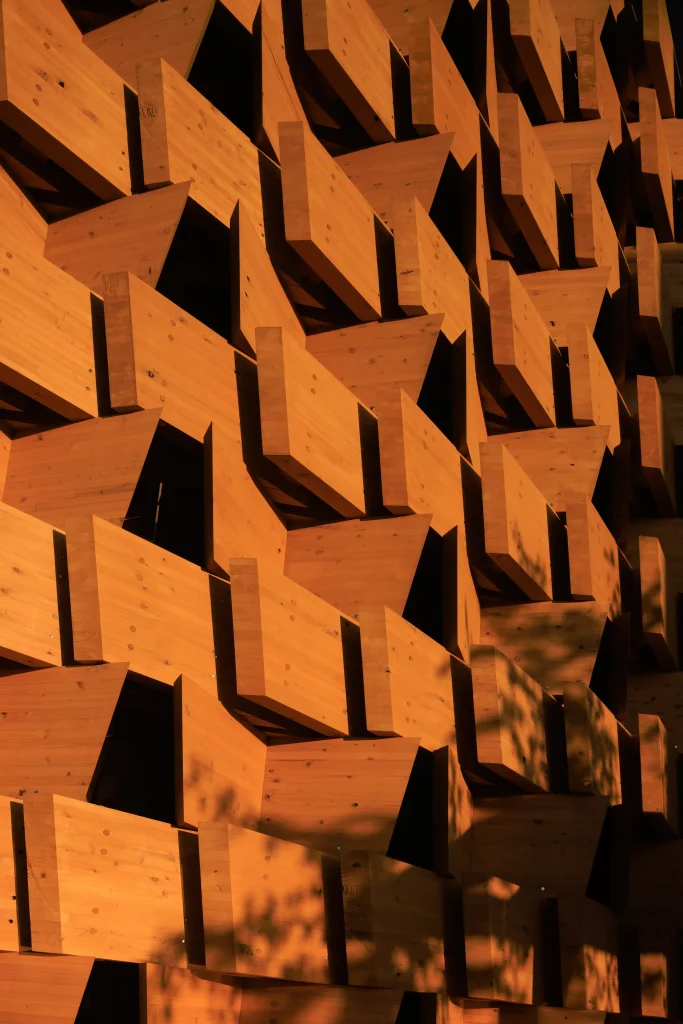 Sunlit close-up of the repeating timber modules and angular voids that give the façade its depth.